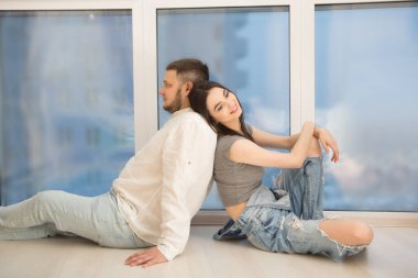 Genç ve mutlu bir çift, apartmanın pencerelerinin yanında, ahşap zeminde oturuyor. 