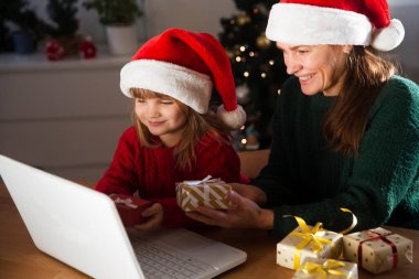 Aile annesi ve kız çocuğu dizüstü bilgisayara ve el sallamaya bakıyor. Arkadaşlarını ya da akrabalarını arayan videolar Noel tatili için evde kalıyor..