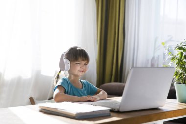 Kulaklıklı kız öğrenci evde video öğretmeniyle bilgisayar kullanıyor ve internetten ders çalışıyor. Evde eğitim, uzak öğrenim