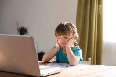 Üzgün kız bir dizüstü bilgisayar kullanıyor ve evdeki video öğretmeniyle internetten ders çalışıyor. Evde eğitim, uzak öğrenim