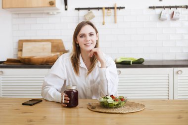 Genç bir kadın evdeki mutfakta öğle yemeğinde yeşil salata yiyor.