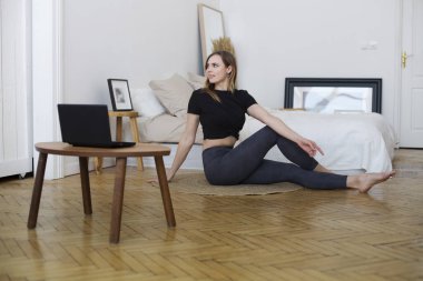 Genç bir kadın evdeki eğitimleri yönetiyor. Uzaktan antrenman. Evden antrenman yapıyorum. ev fitness, aktif giyim.