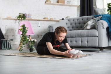 Evdeki odada esneyen ve yoga egzersizi yapan genç bir kadın. Evde fitness, aktif giyim. Sağlıklı ve spor yaşam tarzı. 