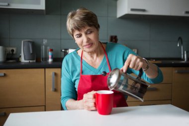 Evde, mutfakta çay içen yaşlı bir kadın..