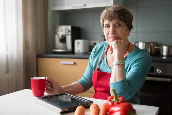 Elegant elderly woman using  tablet in the kitchen