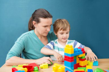 Anne ve küçük oğlu bir sürü renkli plastik blok inşaatçısıyla oynuyorlar. Mutlu aile evde birlikte vakit geçirir..