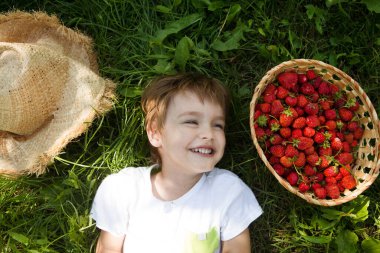 Yazın elinde çilek sepetiyle çimlerin üzerinde uzanan mutlu küçük çocuk. Mutlu küçük çocuk dışarıda eğleniyor..