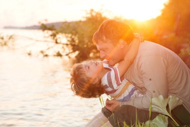 Mutlu baba ve oğul gün batımında nehirde oynuyorlar. Arkadaş canlısı aile kavramı.