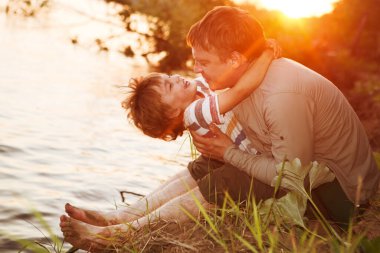 Mutlu baba ve oğul gün batımında nehirde oynuyorlar. Arkadaş canlısı aile kavramı.