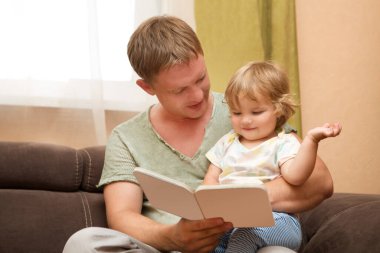 Baba ve çocuk evde kitap okuyarak boş zaman geçiriyorlar.