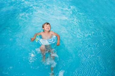 Havuzda lastik halkayla yüzen küçük çocuk, yüzme havuzunda eğleniyor..