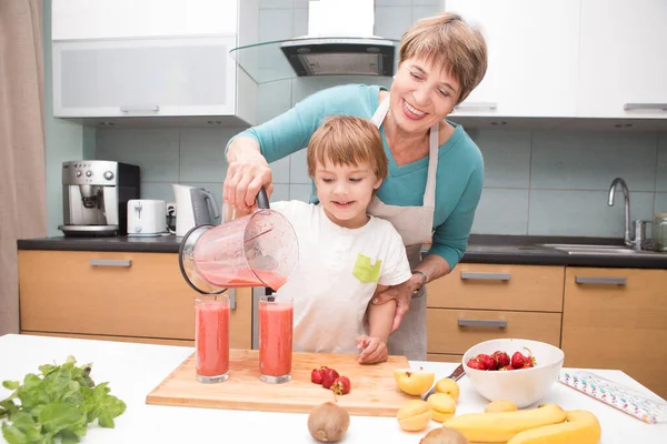 Happy grandmother and little grandson wit fruit smoothie in kitchen. Healthy eating