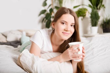Mutlu kız sabahları yatakta kahve içiyor.
