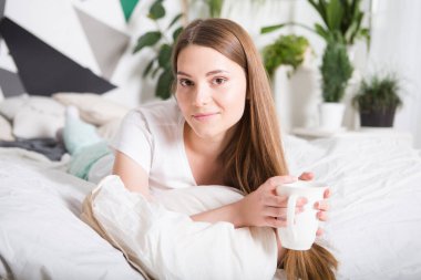 Mutlu kız sabahları yatakta kahve içiyor.