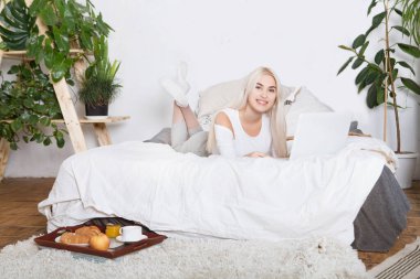 Yatakta dizüstü bilgisayarda çalışan güzel bir genç kadın. Genç ve güzel bir kadın için yatakta kahvaltı