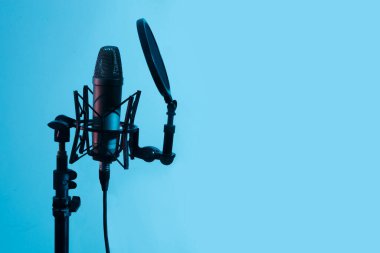 Mavi arka planda A dalgalanması olan profesyonel mikrofon. Podcast veya kayıt stüdyosu arka planı