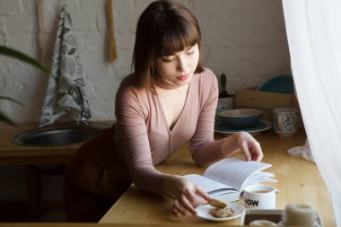 Kız kitap okuyarak ve mutfakta kahve içerek rahatladı.