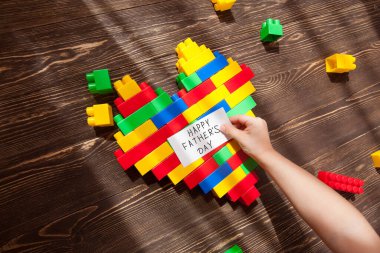 children's hands  holds heart with lots of colorful plastic blocks constructor on a wooden background.  father's day