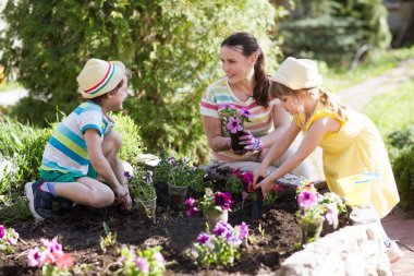 Anne ve iki çocuk bahar günü evin yakınındaki bahçeye çiçek ekerler. Çocuklar anneye bahçede çalışmasında yardım eder. Yavaş yaşam. Küçük şeylerden zevk al.. 