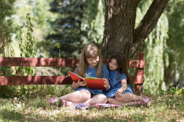 Mutlu çocuklar kitap okuyor ve güneşli yaz gününde bahçede dinleniyorlar. 