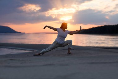 Plajda gün batımında Tai Chi chuan yapan bir kadın. Çin yönetimi yeteneği Qi 'nin enerjisi. tek başına açık hava aktiviteleri. Sosyal Mesafe 