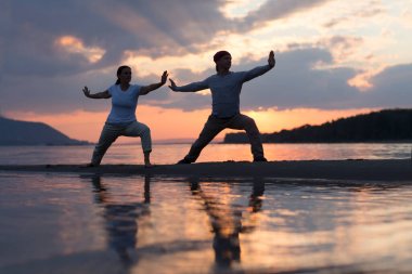 Man and woman doing Tai Chi chuan at sunset on the beach.  solo outdoor activities. Social Distancing. Healthy lifestyle  concept.  clipart