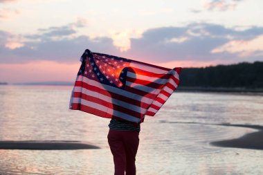 Gün batımında okyanusta Amerikan bayrağı taşıyan bir kadın. Bağımsızlık Günü. ABD 4 Temmuz 'u kutladı.