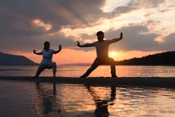 Erkek ve kadın sahilde gün batımında Tai Chi chuan yapıyorlar. tek başına açık hava aktiviteleri. Sosyal Mesafe. Sağlıklı yaşam tarzı kavramı. 