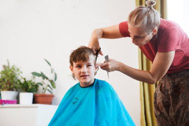 Annem saç stili yapıyor, evde çocuk için saç kesiyor. Sosyal Mesafe. kopyalama alanı. Okul için hazırlık. Makasla kesen kuaför.