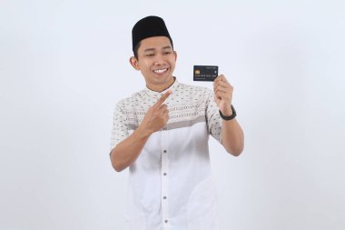 Endonezyalı genç adam gülümsüyor, online alışveriş, e-ticaret ve Ramazan ya da Kurban Bayramı promosyonu sırasında parasız ödeme için kredi kartı gösteriyor..