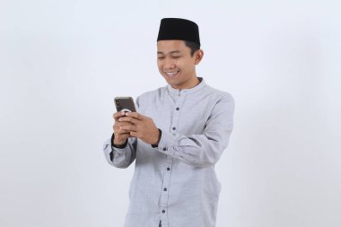 Geleneksel giysiler içinde mutlu bir Asyalı Müslüman erkek portresi cep telefonu kullanıyor, Ramazan ayında sosyal medyada mesajlaşırken ya da gezinirken gülümsüyor..