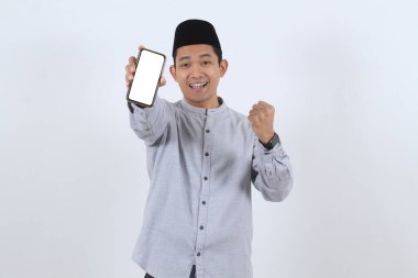 Mutlu Asyalı genç Müslüman adam elinde boş ekranlı bir akıllı telefon tutuyor, Ramazan ya da bayram için bir galibiyet ya da online tanıtım kutluyor..