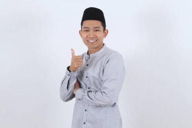 Geleneksel Müslüman kılığına girmiş mutlu Endonezyalı bir adamın portresi onay ya da başarı için başparmak işareti veriyor. Beyaz bir arkaplanda izole edilmiş.