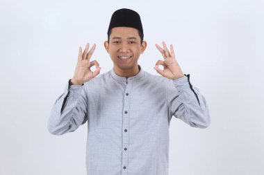 İslami giysiler içindeki mutlu Endonezyalı genç iki eliyle mükemmel bir işaret gösteriyor. Ramazan veya Mübarek Bayramı için olumlu onay ve tatmin kavramı.