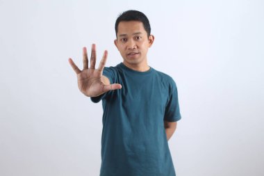 Ciddi Asyalı genç bir adam avuç içi göstererek uyarı ya da dur işareti yapıyor. İnkar etme, reddetme, sınırlar koyma ya da hayır deme kavramı. İzole edilmiş portre.