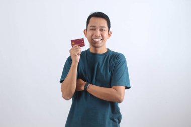 Kredi kartını gösteren kendine güvenen genç Asyalı bir adamın portresi. Mutlu müşteri kolay ödeme, çevrimiçi alışveriş ve finans hizmetlerinden zevk alıyor.