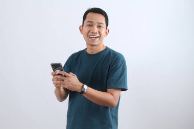 Neşeli yetişkin Endonezyalı adam cep telefonu kullanıyor, mutlu ve başarılı hissediyor. Dijital iletişim, sosyal medya ve müşteri memnuniyeti kavramı.