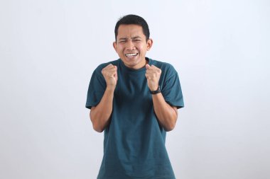 Yumruklarını sıkan, neşeli ve başarılı ya da son derece sinirli ve stresli genç Asyalı bir adamın portresi. İzole edilmiş.