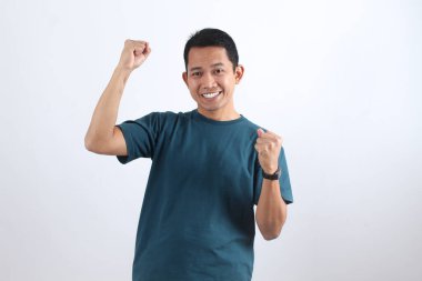 Neşeli Asyalı adam bir başarıyı kutlayarak heyecan ve zafer ifade ediyor. Beyaz arka planda izole edilmiş başarılı bir kazananın portresi.