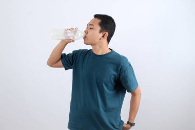 Sağlıklı genç bir adam susuzluğunu gideriyor. Susuzluğunu gidermek için bir şişeden saf su içiyor. Kopyalama alanı olan beyaz bir arkaplanda izole edilmiş.