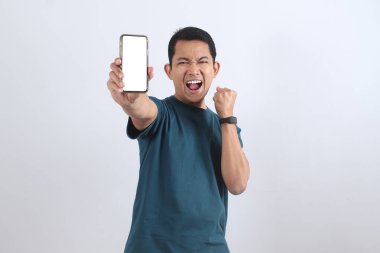 Neşeli Asyalı genç adam mutlulukla bağırıyor uygulamanız ya da web siteniz için beyaz ekranlı bir akıllı telefon tutuyor. Başarı ve başarı kavramı.