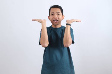 Sıradan tişörtlü mutlu genç adam avuçları arasında bir seçim ya da görünmez bir nesne sunar. Ürün yerleştirme veya metin için beyaza izole edilmiş.