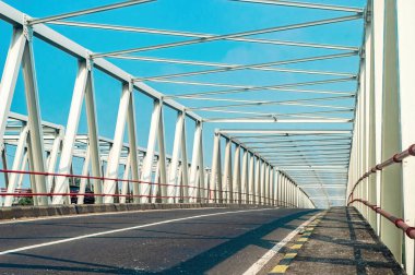 Modern bir çelik köprü, Endonezya 'nın Doğu Java kentindeki Brantas Nehri' ni berrak mavi gökyüzünün altında kaplar. Tropik bir arazide kentsel gelişim, ulaşım ve mühendislik gösteren ikonik bir yapı.