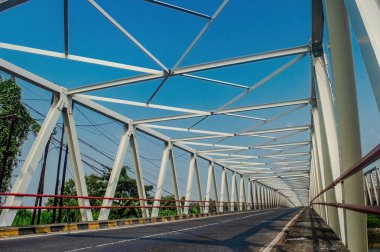 Endonezya 'nın Doğu Java kentindeki Brantas Nehri boyunca uzanan çelik kiriş köprüsü, parlak bir gökyüzünün altında sağlam beton sütunlarla desteklenmektedir. Altyapı, ulaşım ve seyahat temaları için ideal