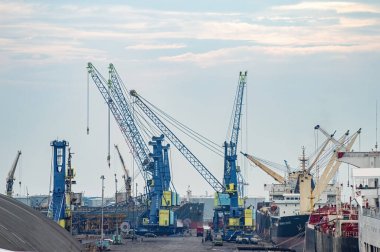 Kargo gemileri bulutlu bir gökyüzüne karşı büyük mavi vinçlerle Tanjung Perak limanına yanaştı. Liman sahnesinde uluslararası ticaret ve lojistik, Endonezya, 14 Kasım 2025.