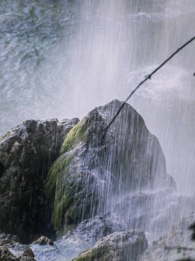 Hırvatistan 'ın Plitvice Göllerindeki bir şelalenin yakın görüntüsünde, düşen su perdesinin arkasında yosunlu kayalar beliriyor.