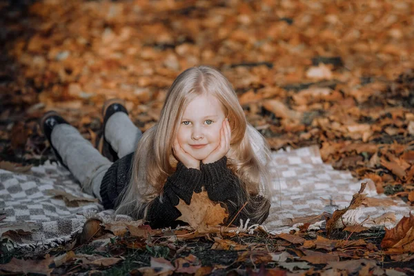 blonde girl lies on a blanket in the park in autumn