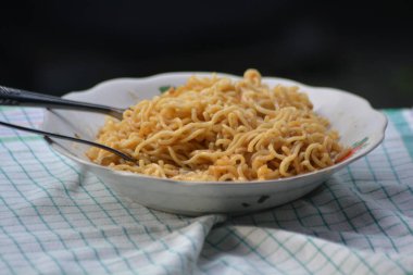 Metal kaşık ve çatalla çiçek desenli bir tabakta hazır erişte, damalı kumaş üzerinde servis edilen ev tarzı.