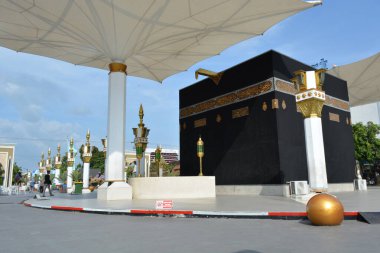 15 Haziran 2025 'te Madiun Endonezya' da dekore edilmiş sütunlar ve gölge şemsiyelerle çevrili yükseltilmiş bir platformdaki Kabe kopyasının geniş görünümü