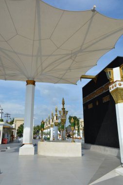 Bakış açısı, 15 Haziran 2025 'te İslami temalı bir plaza Madiun Endonezya' daki Kabe kopyası ve hizalı sütunlara yönelik geniş bir gölge şemsiyesini geçerek,